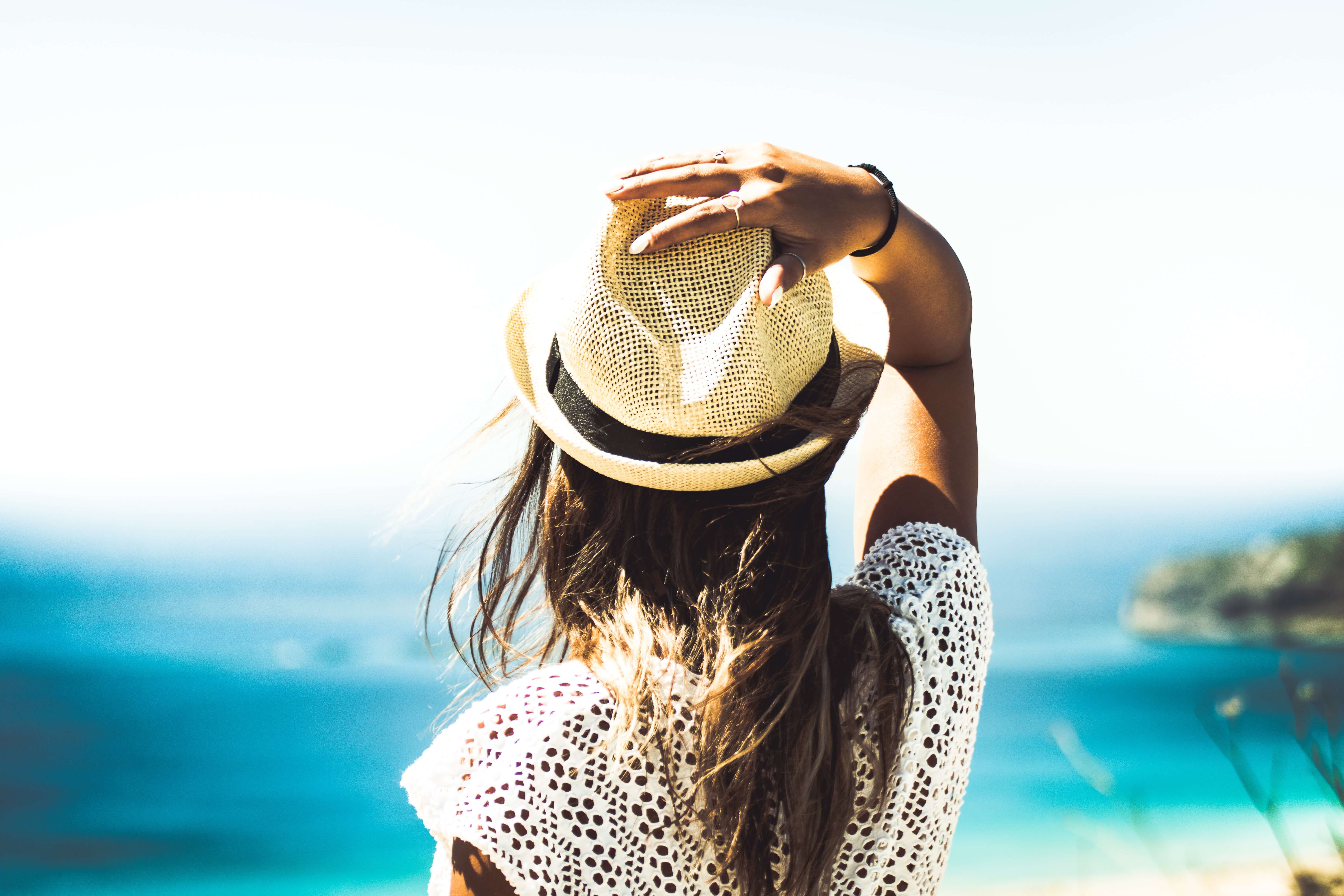 a girl with a straw hat facing the sea